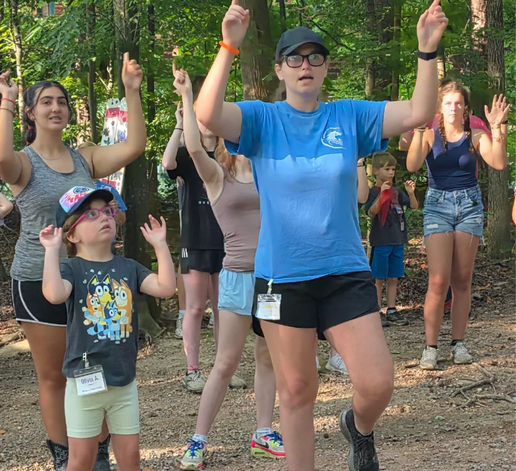 Volunteers and children participate in a group activity with raised hands during a camp program at Wings of Eagles Ranch.